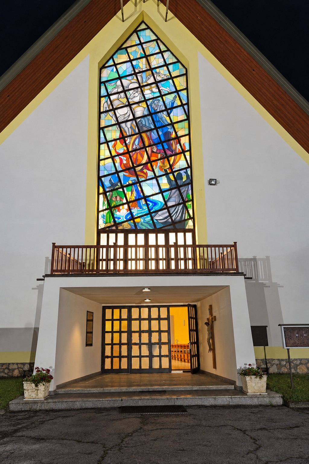 The facade of the church in Garevac at night, with the stained glass window lit from within above the entrance
