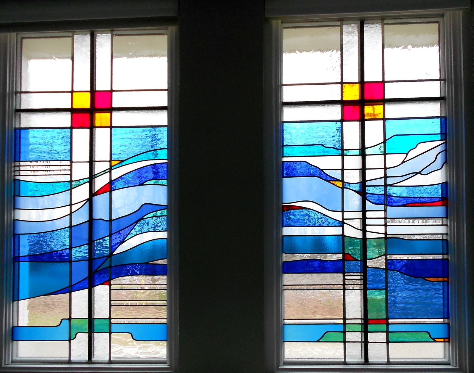 2 stained glass windows by Brenda Belfield at Heritage Fellowship Church, Reston, Virginia: a clear glass cross with red and gold squares rising through waves of blue