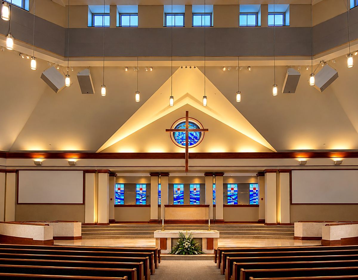 Sanctuary of Heritage Fellowship Church, Reston, Virginia, with the round stained glass window behind the altar cross and blue stained glass windows behind the platform