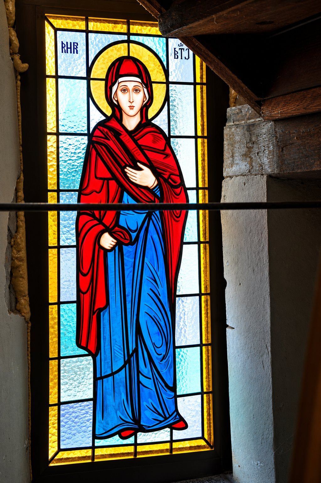 Stained glass window of a female saint in a red mantle over a blue robe, Greek Catholic church in Mikluševci