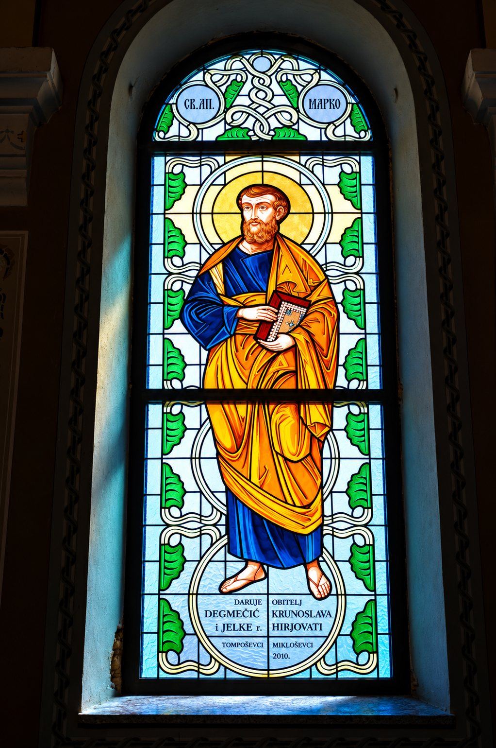 Stained glass window of Saint Mark the Evangelist in a gold mantle with his Gospel, Greek Catholic church in Mikluševci