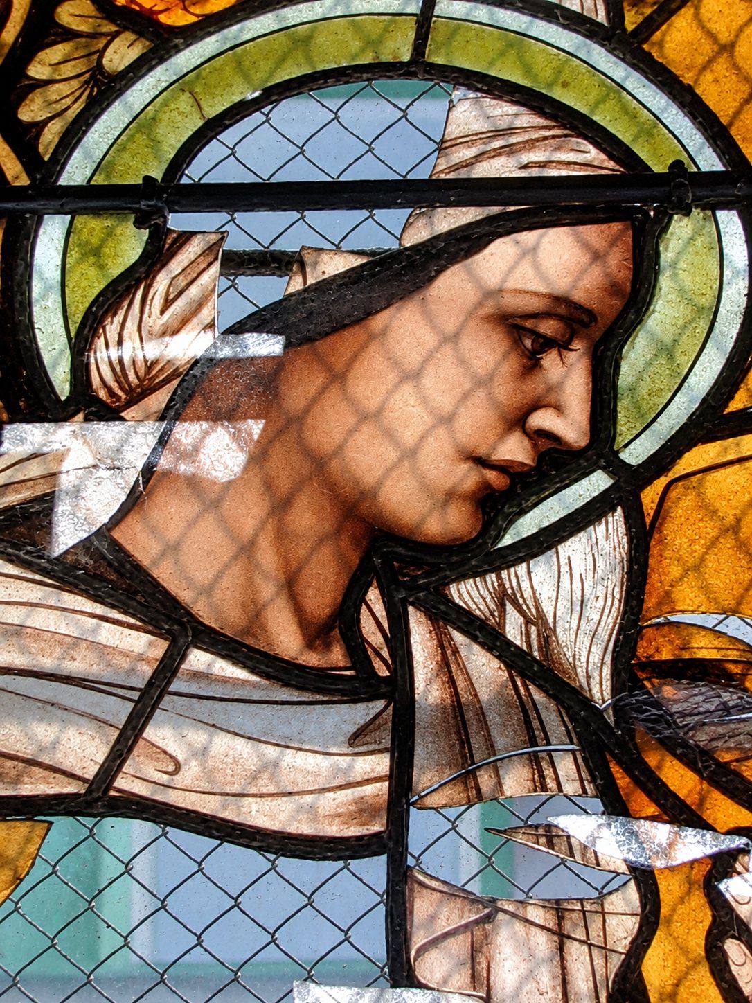 War damaged stained glass detail of an angel's face behind wire mesh, Saint Joseph, Sarajevo
