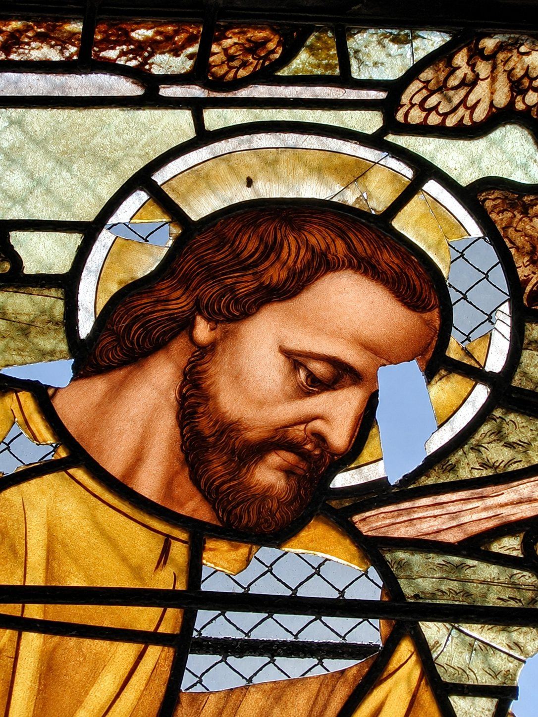 War damaged stained glass detail of a saint's face with missing glass behind wire mesh, Saint Joseph, Sarajevo