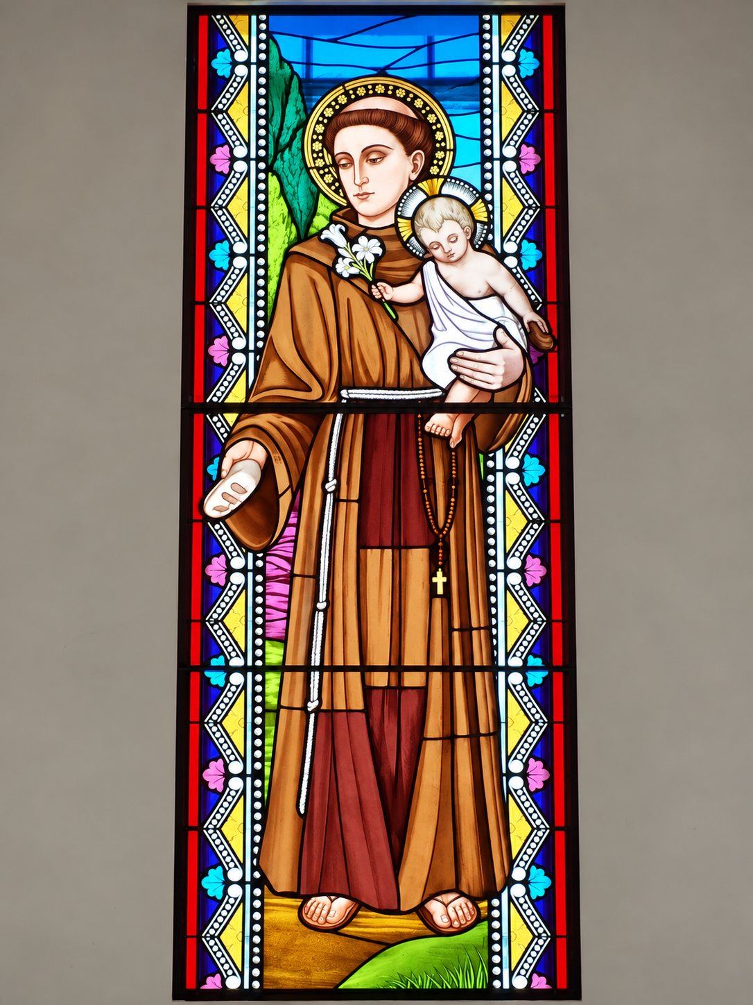 Stained glass window of Saint Anthony of Padua with the Christ Child, a lily and a rosary, Pastoral Centre in Tuzi