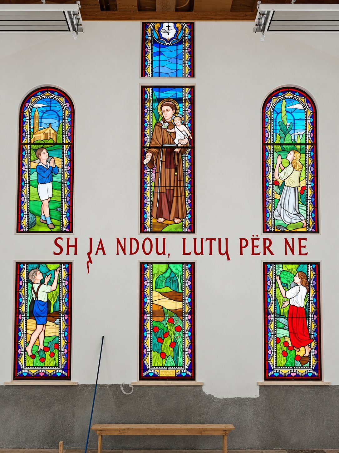 The stained glass wall with Saint Anthony in the center and the words Shna Ndou, lutu për ne, Pastoral Centre in Tuzi