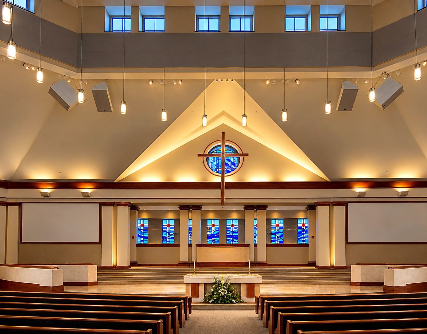 Sanctuary of Heritage Fellowship Church, Reston, Virginia, with the round stained glass window behind the altar cross and a row of blue stained glass windows behind the platform