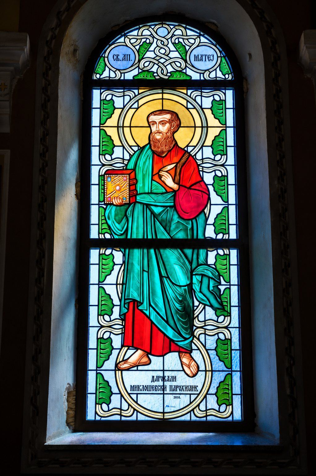 Stained glass window of Saint Matthew the Evangelist in a green mantle with his Gospel, Greek Catholic church in Mikluševci